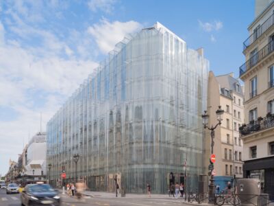 En partie haute, le pan coupé de l'étage-attique et les émergences techniques compromettent à chacun des deux angles l'immatérialité évanescente de la splendide façade conçue par Sanaa (© Jared Chulski)