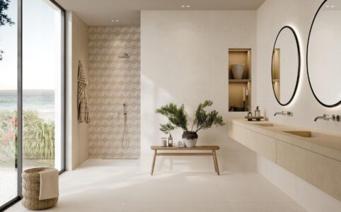 Sofisticato ambiente bagno. A pavimento la finitura Ivory 120x120, sulla parete lavabo spicca Docks, nella finitura Ivory. Si tratta di un motivo decorativo (30x60cm) che alterna formati rettangolari differenti, per aggiungere dinamismo e originalità alle superfici. Il lavabo è rivestito con Grace Beige, nel grande formato 120x278. La parete doccia è realizzata con il Mosaico Rombi (30,5x35,2), variante White Ivory, che crea un effetto ottico tridimensionale