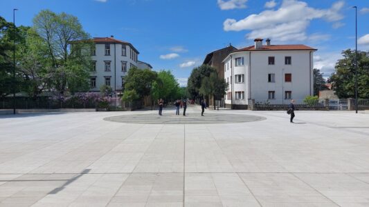 Nova Gorica: vista del piazzale di ingresso storico alla stazione Transalpina, con il cerchio a terra che segna l’ex linea di confine e sullo sfondo Gorizia (© Lucia Krasovec-Lucas)